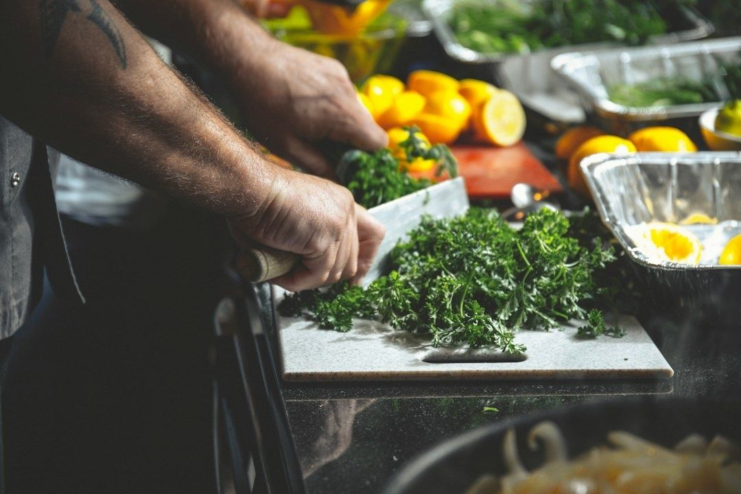 Chef chopping fresh parsley beside colorful vegetables in a kitchen