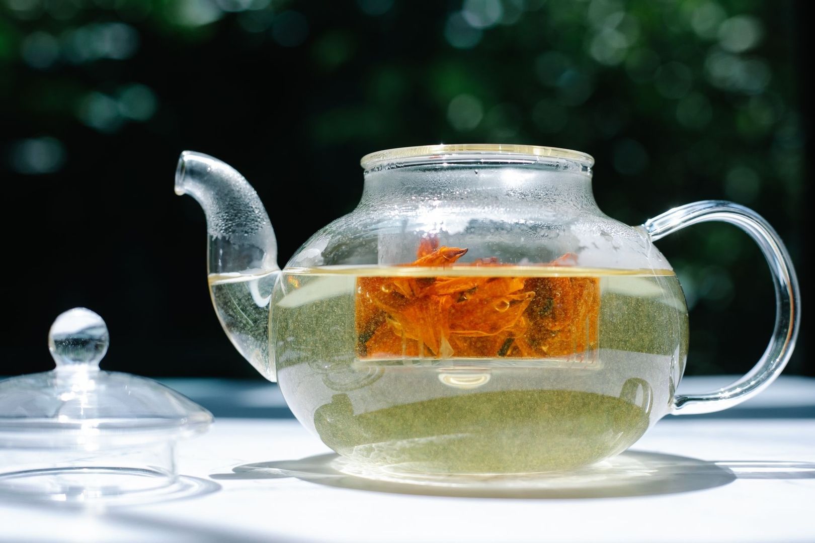 Glass teapot of pale tea with orange botanicals on a table
