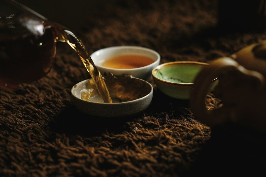 Tea being poured into a small tasting bowl beside other tea cups